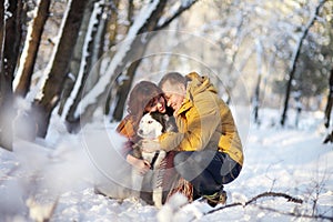 Couple smiling and having fun in winter park with their husky dog