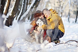 Couple smiling and having fun in winter park with their husky dog