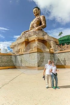 Couple smiling near giant Buddha Dordenma statue with the blue sky and clouds background, Thimphu, Bhutan