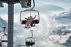 Couple snowboarders having fun on a ski lift in ski resort with beautiful background of snow-covered slopes, hills