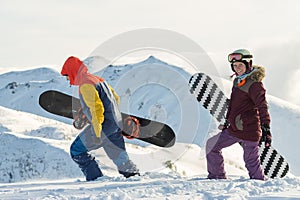 Couple snowboarding freeriders man and a woman go with snowboards on the ridge