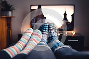 Couple with socks and woolen stockings watching movies or series on tv in winter. Woman and man sitting or lying together on sofa.