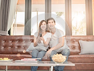 Couple on sofa with TV remote watching television in living room