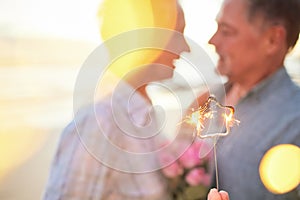 Couple, sparkler and date to celebrate love, birthday and vacation or holiday at beach in summer. Senior man and woman