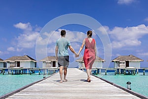 Couple spending romantic beach vacation holidays at luxurious resort in Maldives with overwater villas, turquoise sea water and