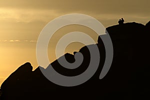 A couple stand silhouetted against a sunset atop stanage edge