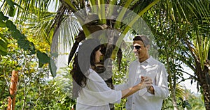 Couple Stand Under Palm Tree Kiss Talking In Tropical Garden , Happy Man And Woman Outdoors