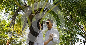 Couple Stand Under Palm Tree Kiss Talking In Tropical Garden , Happy Man And Woman Outdoors