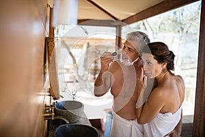 Couple standing with arm around while shaving in cottage