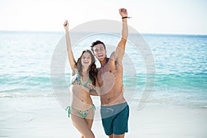 Couple standing with arms raised at beach