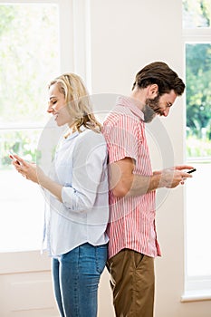 Couple standing back to back and text messing on mobile phone