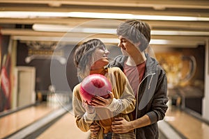 Couple standing in a bowling alley and holding a ball together.