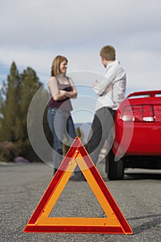 Couple Standing By Breakdown Car With Warning Triangle In Foreground