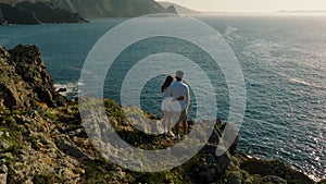 Couple Standing On Cliff Overlooking The Ocean On The Atlantic Coast. Aerial pullback