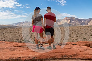 Couple standing on edge of Calico Hills cliff with scenic view of limestone peaks Mount Wilson and Rainbow Mountain