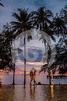 Couple standing on the edge of an infinity pool watching the sunset under the huge palm trees