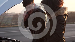 Couple standing near broken car and calling for help on phone