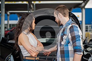 Couple standing near a broken car outdoors and looking at the engine, hood open. Car service, insurance, transportation