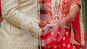 Couple standing together dressed in traditional Indian clothes and holding hands, hindu wedding. Close up