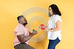 Couple standing together, man making proposal to his girlfriend woman showing red stop sign refusing