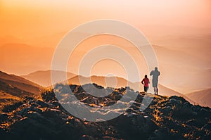 Couple standing on the top of the hill on the mountains meadow with beautiful colorful sunset over landscape