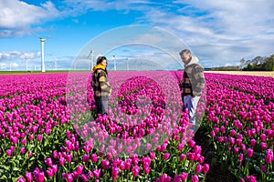 A couple stands gracefully in a vibrant field of purple tulips, surrounded by the beauty of windmill turbines in the