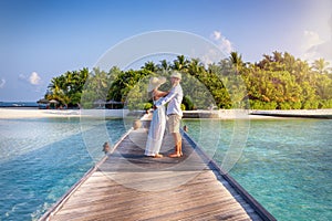A couple stands hugging on a wooden pier over turquoise sea in the Maldives