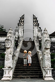 A couple stands on the stairs of the Baltic temple and cover their faces with rice caps. Man and woman traveling in Indonesia.