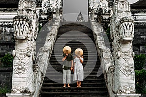 A couple stands on the stairs of the Baltic temple and cover their faces with rice caps. Man and woman traveling in Indonesia.