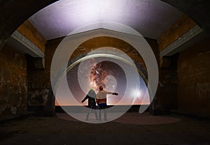 Couple stands under arch in the night. Couple in love looks at the bright milky way galaxy.