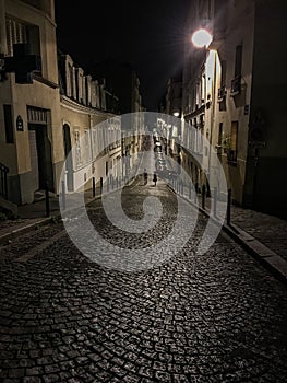 A couple strolls in the distance down a cobbled Paris street at night