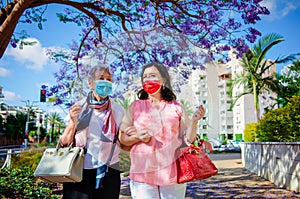 A couple of stylish elderly ladies walk against the background of a blooming jacaranda tree.