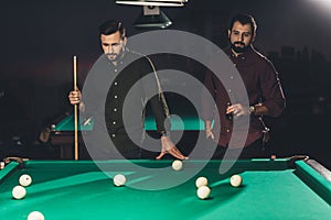 couple of successful men standing beside pool table with drink