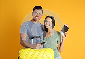 Couple with suitcase and tickets in passports for summer trip on yellow background. Vacation travel