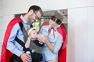 Couple in superhero costume feeding milk to daughter