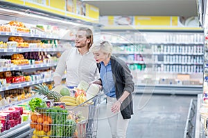 Couple in a supermarket shopping with full food cart buying groceries