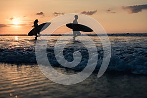 Couple of surfers walking on coastline at sunset