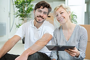 couple with tablet sitting on floor at new apartment