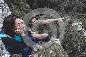 Couple taking a break while hiking, sitting at a viewpoint, pointing and looking at distance