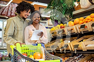 Couple Taking Notes In Shopping List Buying Food In Supermarket