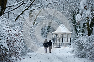 couple taking a romantic walk in a snow-covered park, with a gazebo in the background