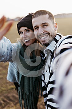 Couple taking a selfie photo in countryside at sunset. Focus on man