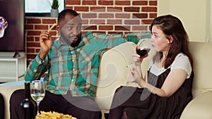 Couple talking on couch, consuming drinks and snacks at social reunion after catching up with mates