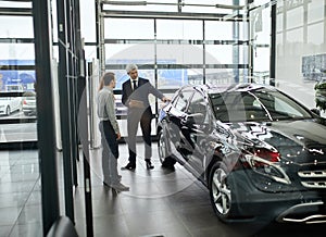 Couple talking with mature sales manager while choosing a car in dealership