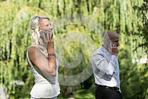 Couple talking on mobile or smart phone. Man and woman speak with telephone. Young people use cellphone for call in park.