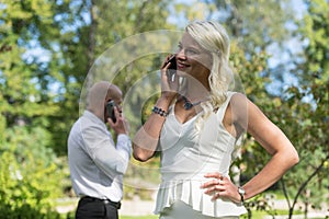 Couple talking on mobile or smart phone. Man and woman speak with telephone. Young people use cellphone for call in park.