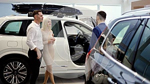 Couple talking to car dealer in dealership discussing automobiles looking at luxurious new white model