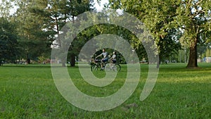 A couple on a tandem bike rides through the park between the trees