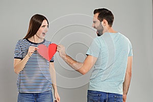 Couple tearing paper heart on grey background. Relationship problems