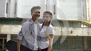 Couple of teens with skateboard looking at camera and smiling, youth subculture